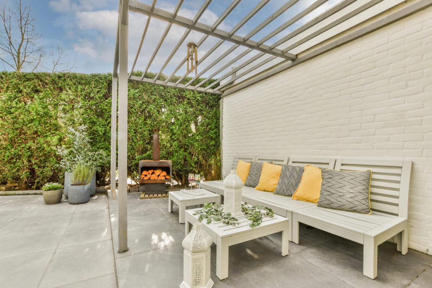 A patio with a couch , table and fireplace under a pergola.