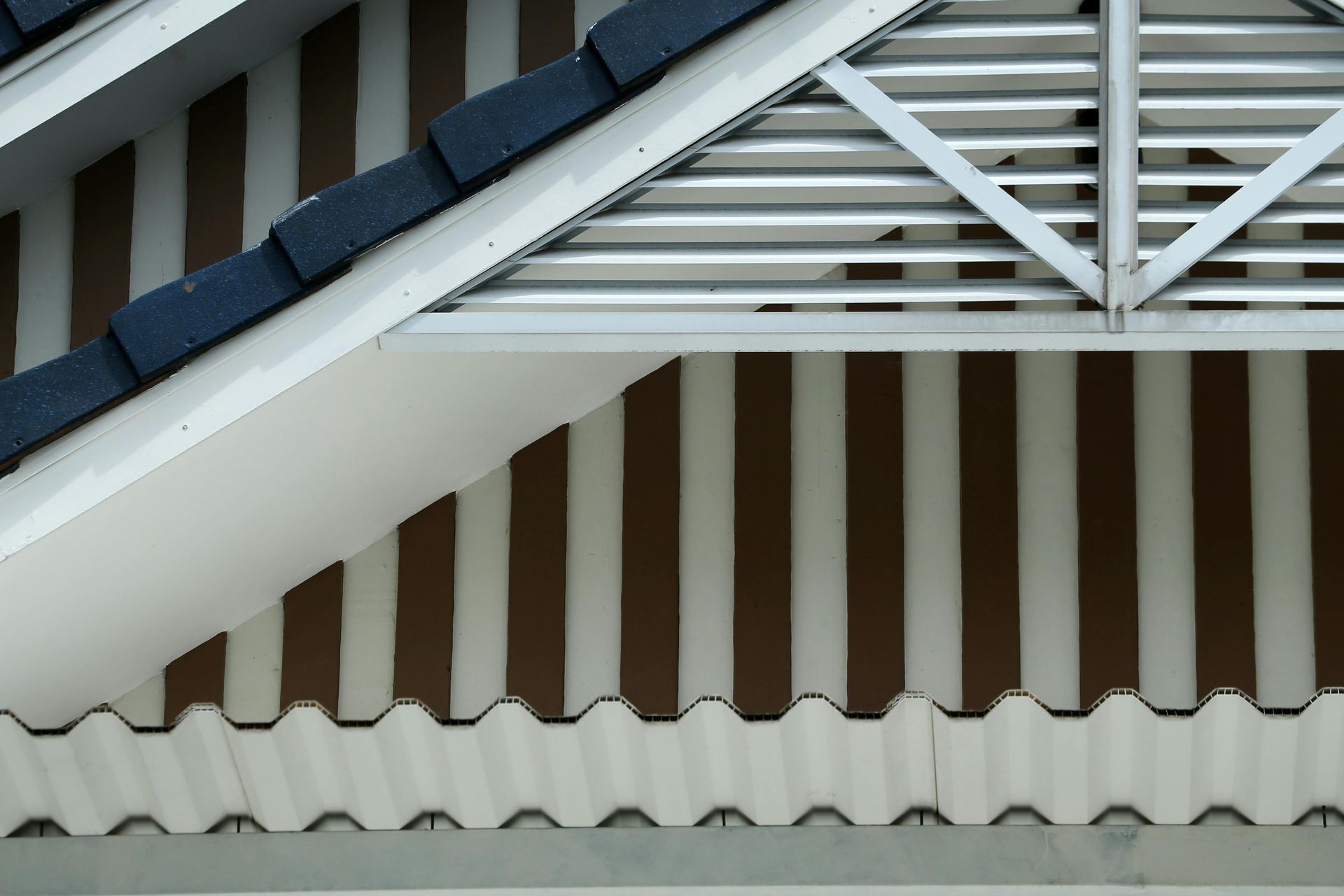 Close-up of a house roof with dark blue shingles, white trim, and brown vertical slats.