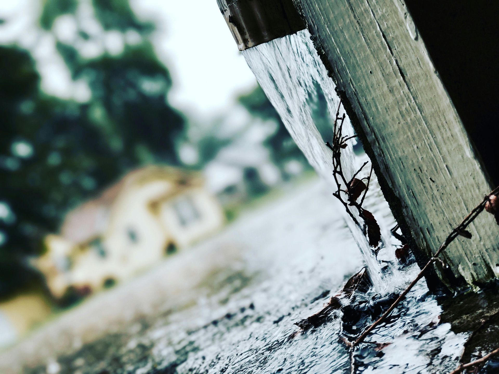 Rainy day view from under a wet wooden overhang, blurred house in background.