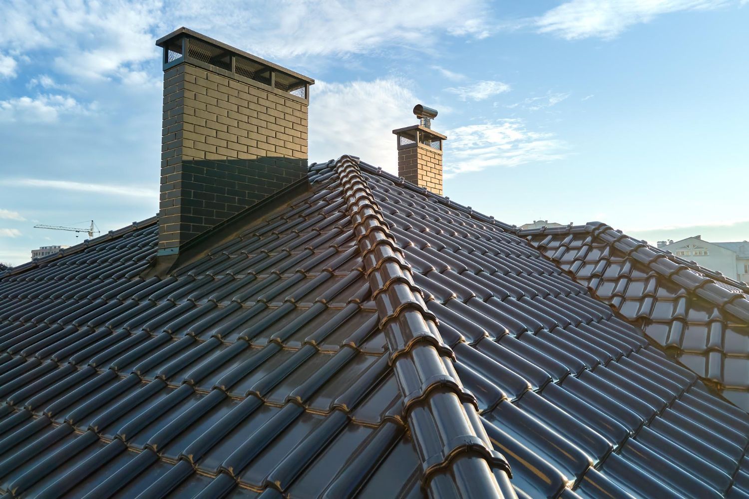 Dark tiled roof with two brick chimneys against a blue sky.