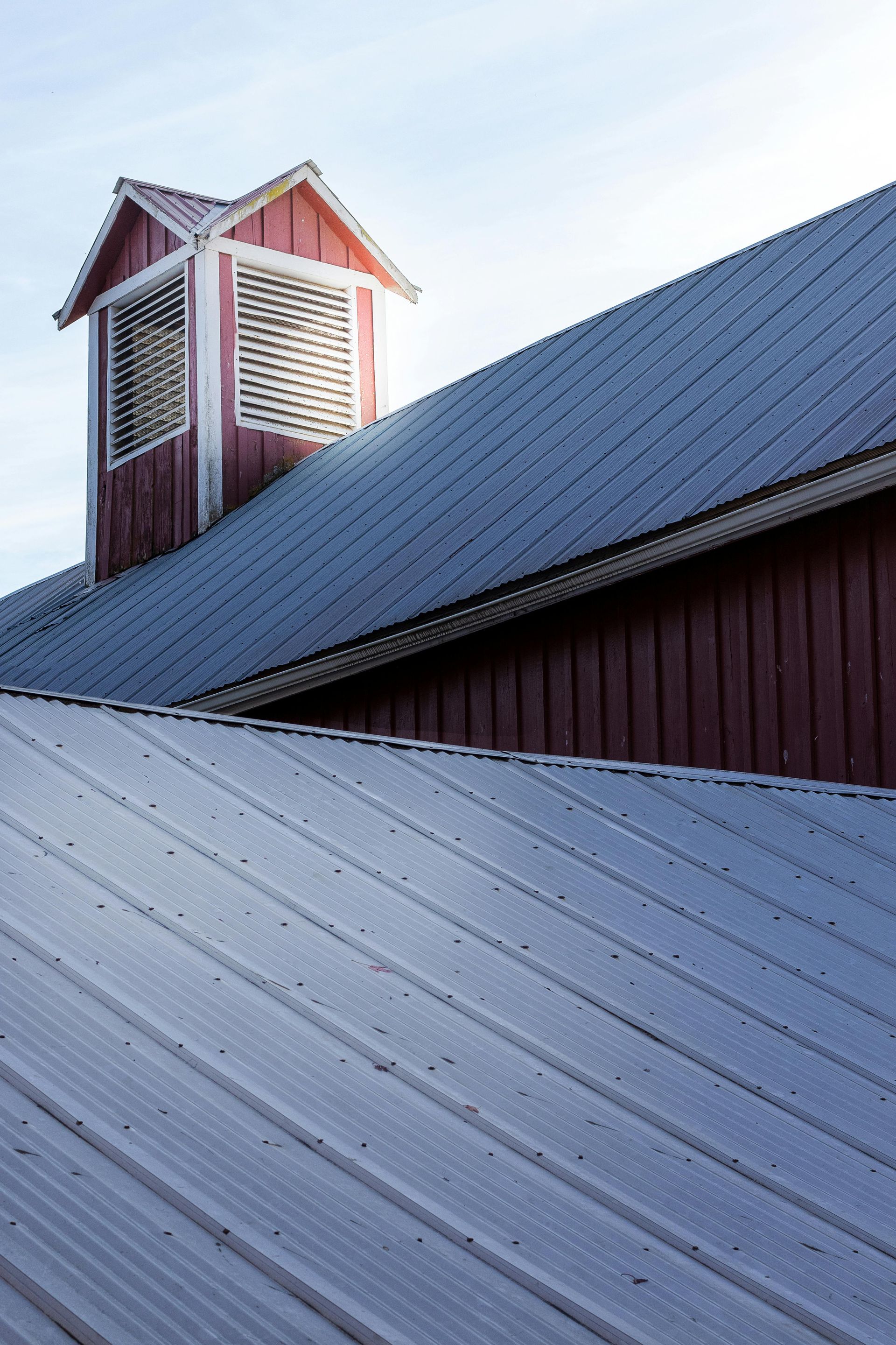 Red barn with a metal roof and a cupola against a blue sky.